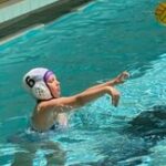 Young girl in water polo cap throwing ball.